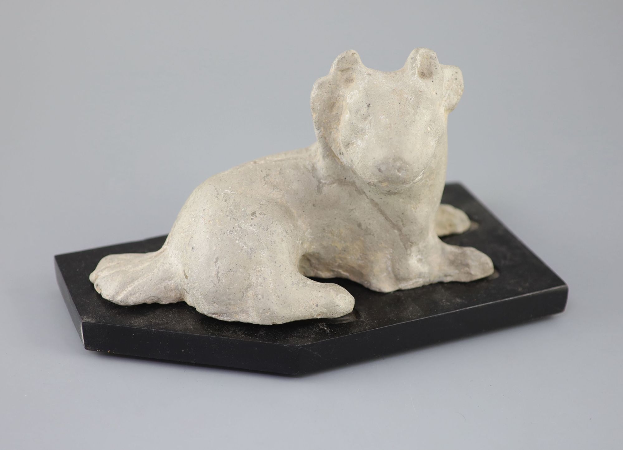 A Chinese grey pottery figure of a recumbent dog, Han dynasty or later 23.5cm long, wood stand